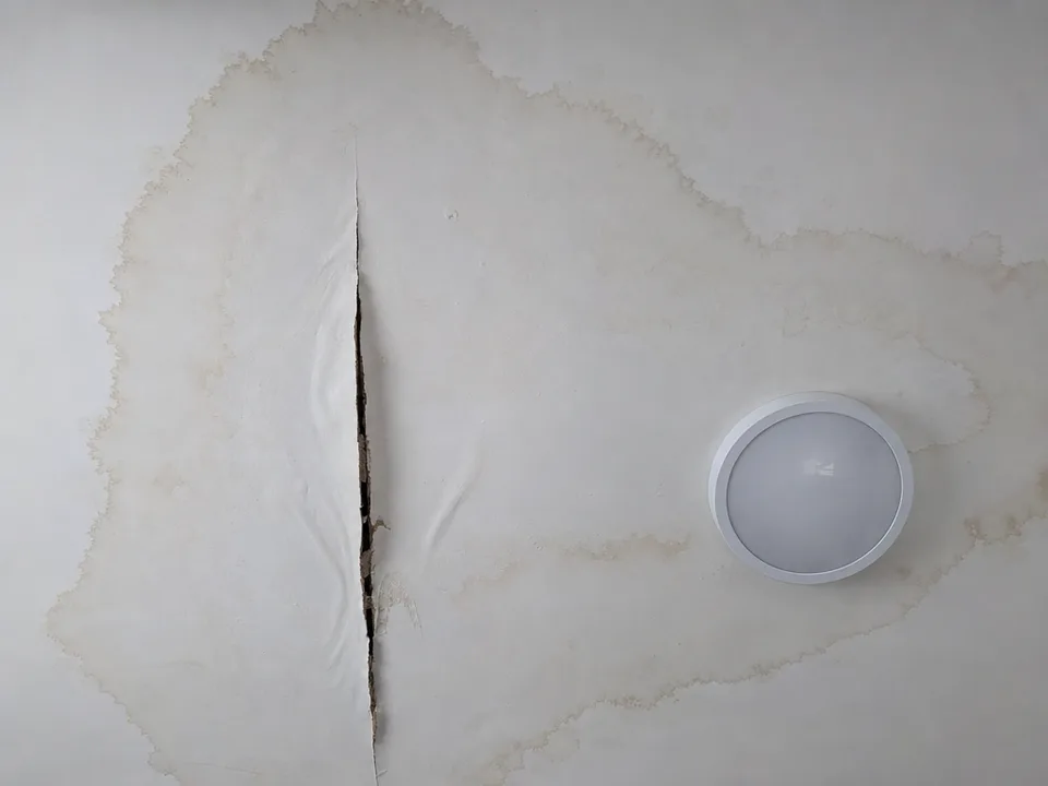 Looking straight up at a white drywall ceiling with a brown water stain and a sagging, split seam